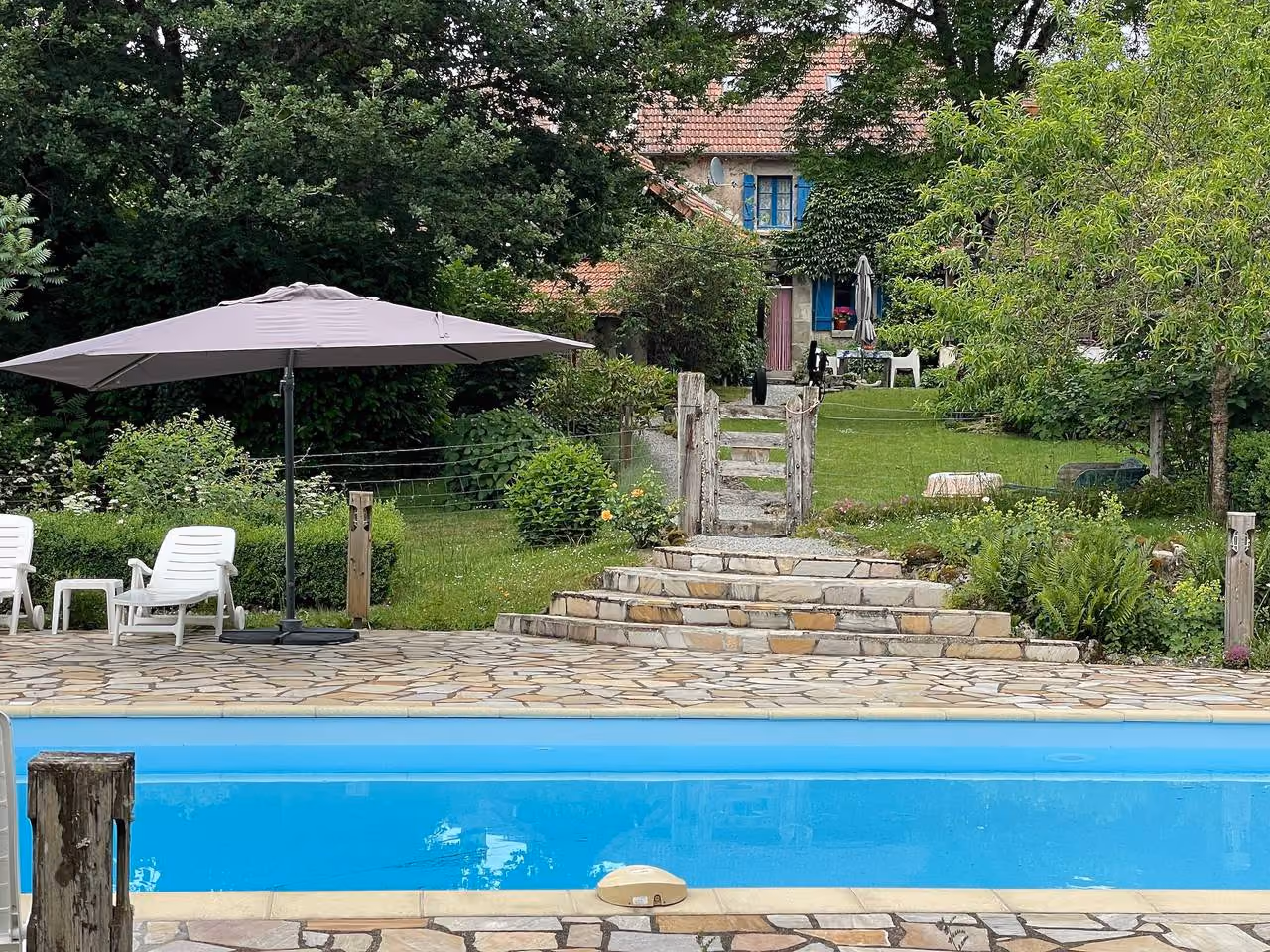 Overzicht van het zwembad met parasols, het huis op de achtergrond tussen de bomen